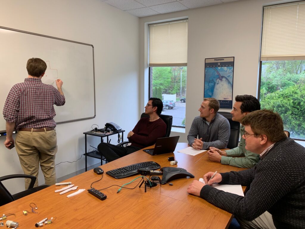 Man writing on whiteboard while others sit at table